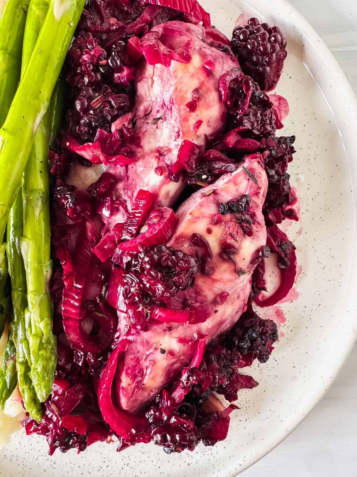 blackberry chicken with asparagus on a white plate.