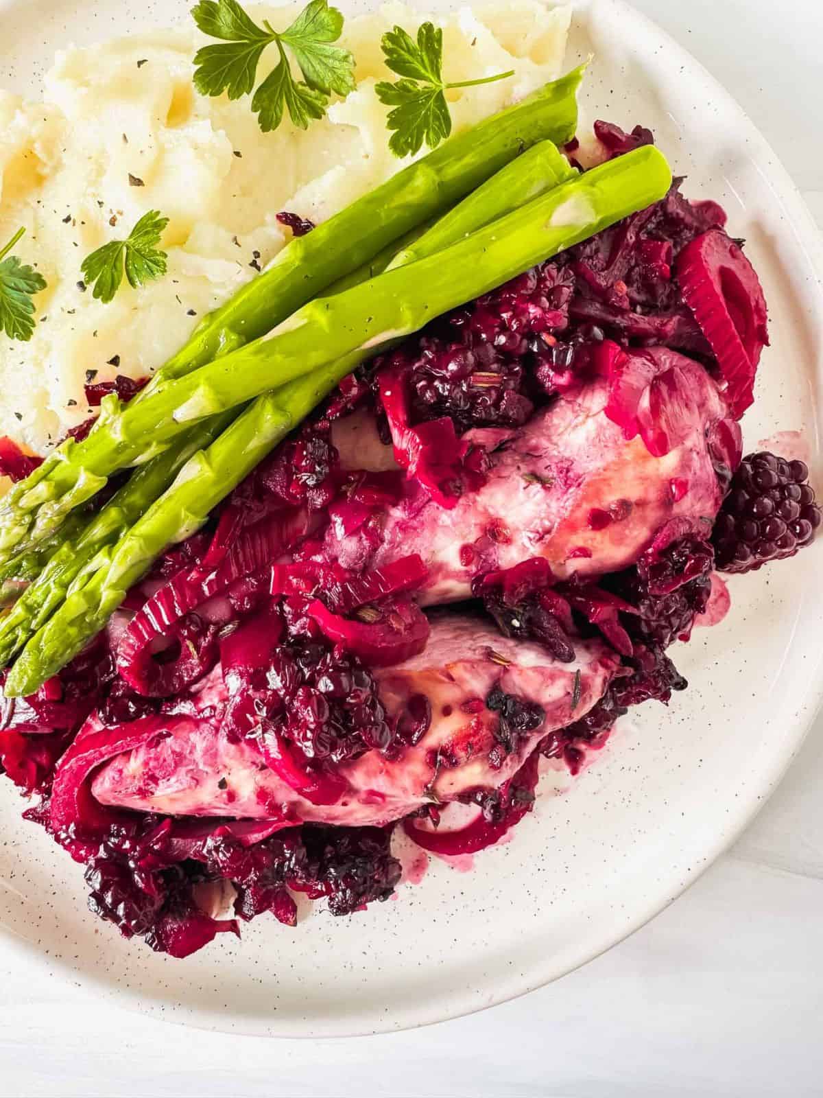 blackberry chicken with mashed potatoes and asparagus on a white plate.
