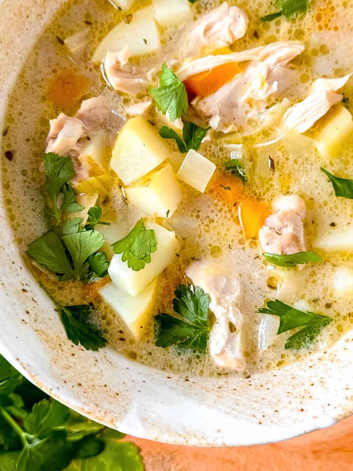 chicken leek potato soup in a bowl garnished with fresh parsley leaves.