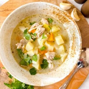 chicken leek potato soup in a bowl next to fresh parsley and garlic cloves.