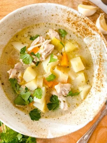 chicken leek potato soup in a bowl next to fresh parsley and garlic cloves.