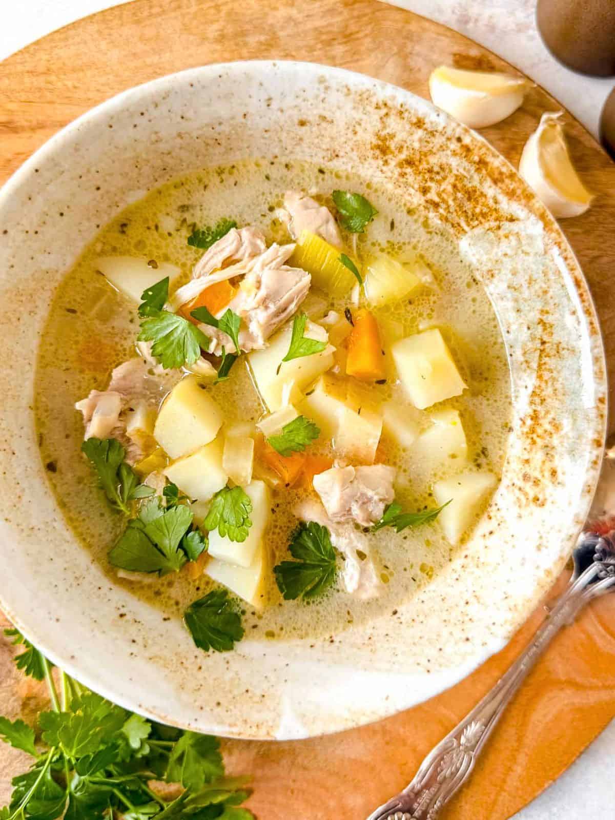 chicken leek potato soup in a bowl next to fresh parsley and garlic cloves.
