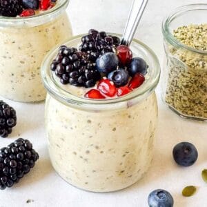 hemp seed overnight oats in glass jars topped with fruit next to a jar of hemp seeds.