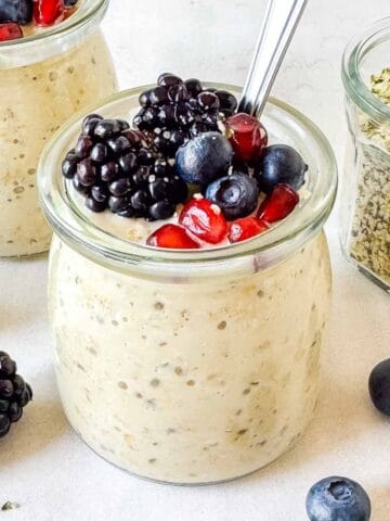 hemp seed overnight oats in glass jars topped with fruit next to a jar of hemp seeds.