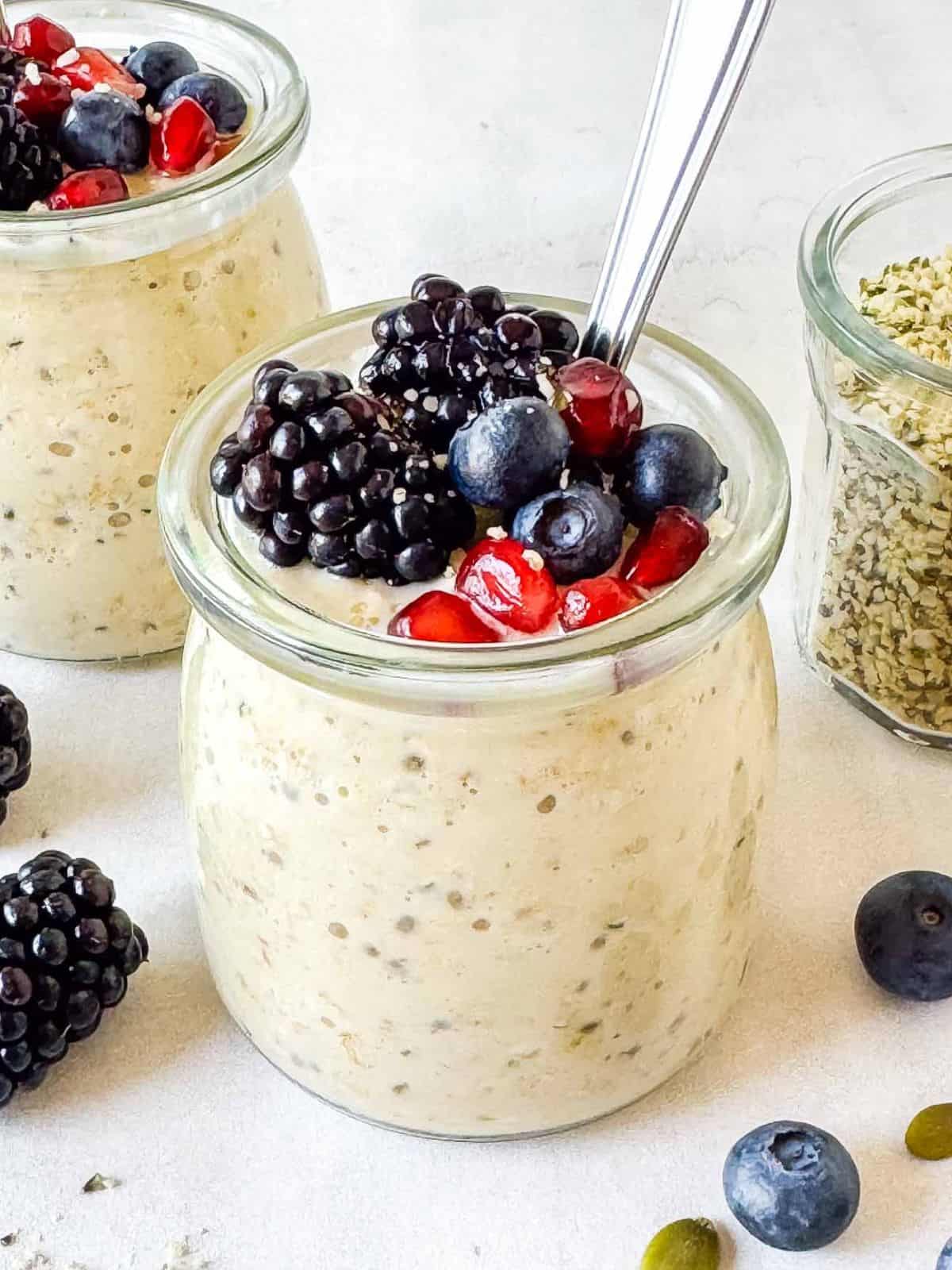 hemp seed overnight oats in two glass jars next to a jar of hemp seeds and fresh berries.