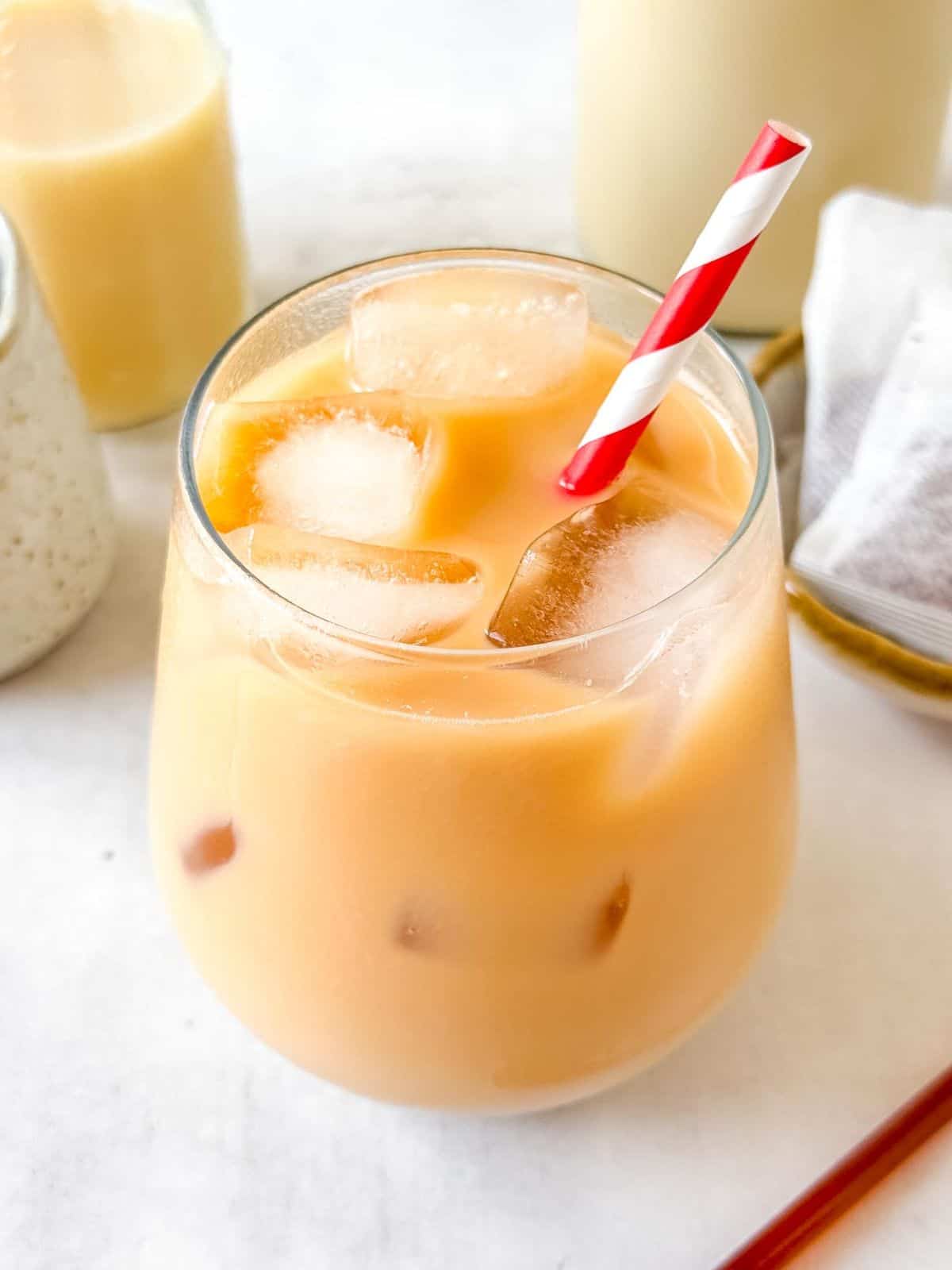 iced rooibos tea latte in a glass next to bottles of milk and tea bags.