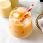 iced rooibos latte in a glass with a red and white straw next to bottles of milk and tea bags.
