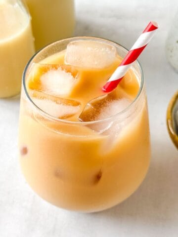 iced rooibos latte in a glass with a red and white straw next to bottles of milk and tea bags.