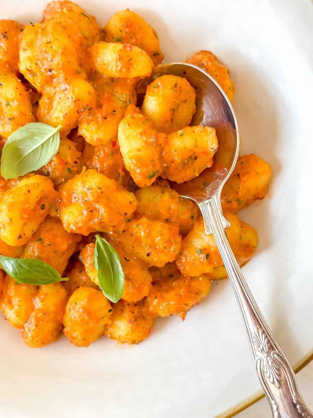 roasted red pepper gnocchi in a white bowl with a spoon.