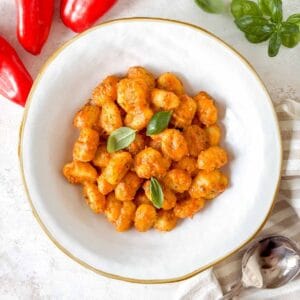 roasted red pepper gnocchi in a white bowl garnished with fresh basil leaves.