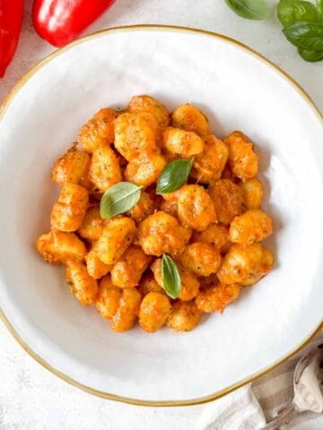 roasted red pepper gnocchi in a white bowl garnished with fresh basil leaves.