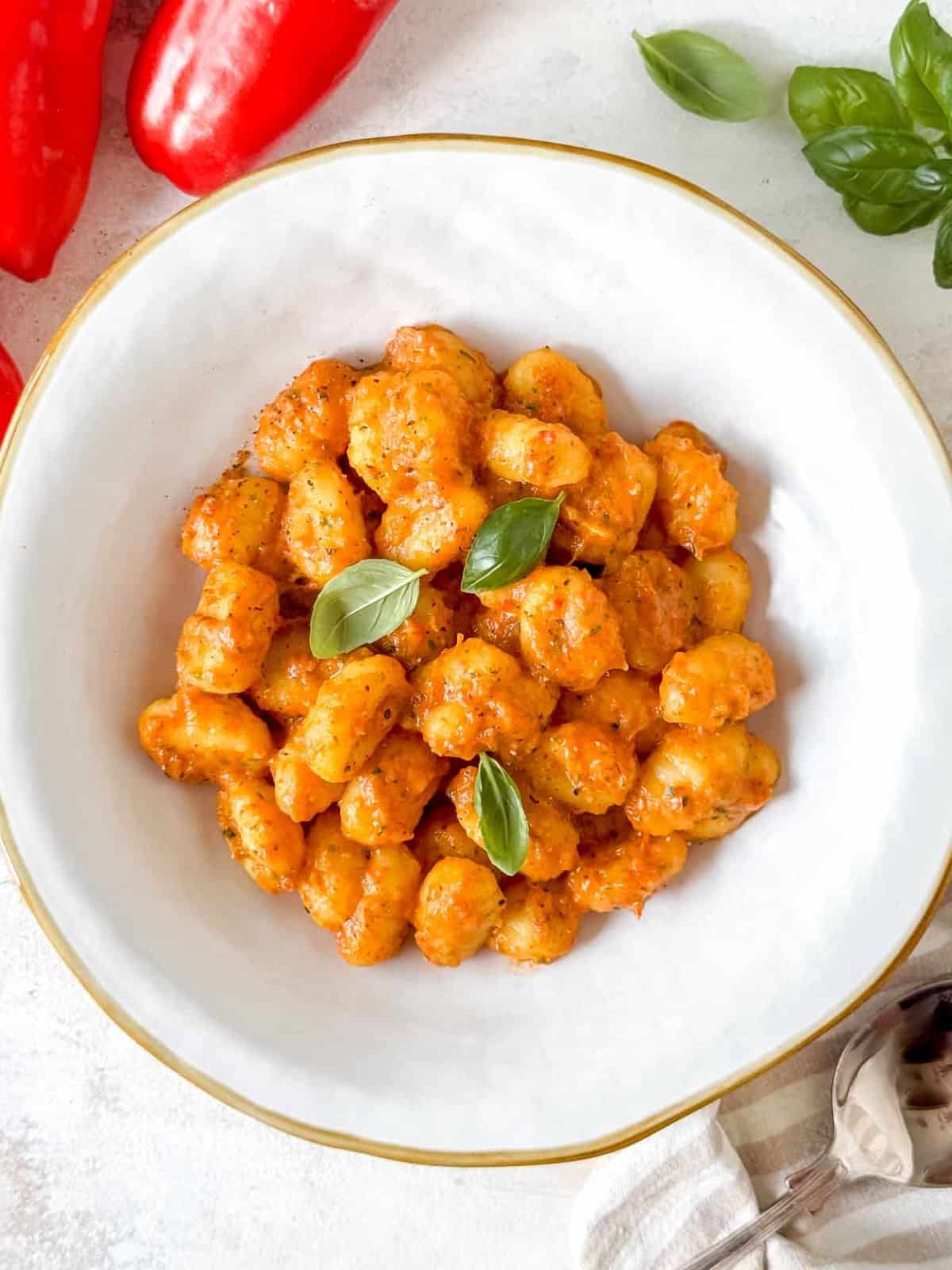 roasted red pepper gnocchi in a white bowl garnished with fresh basil leaves.