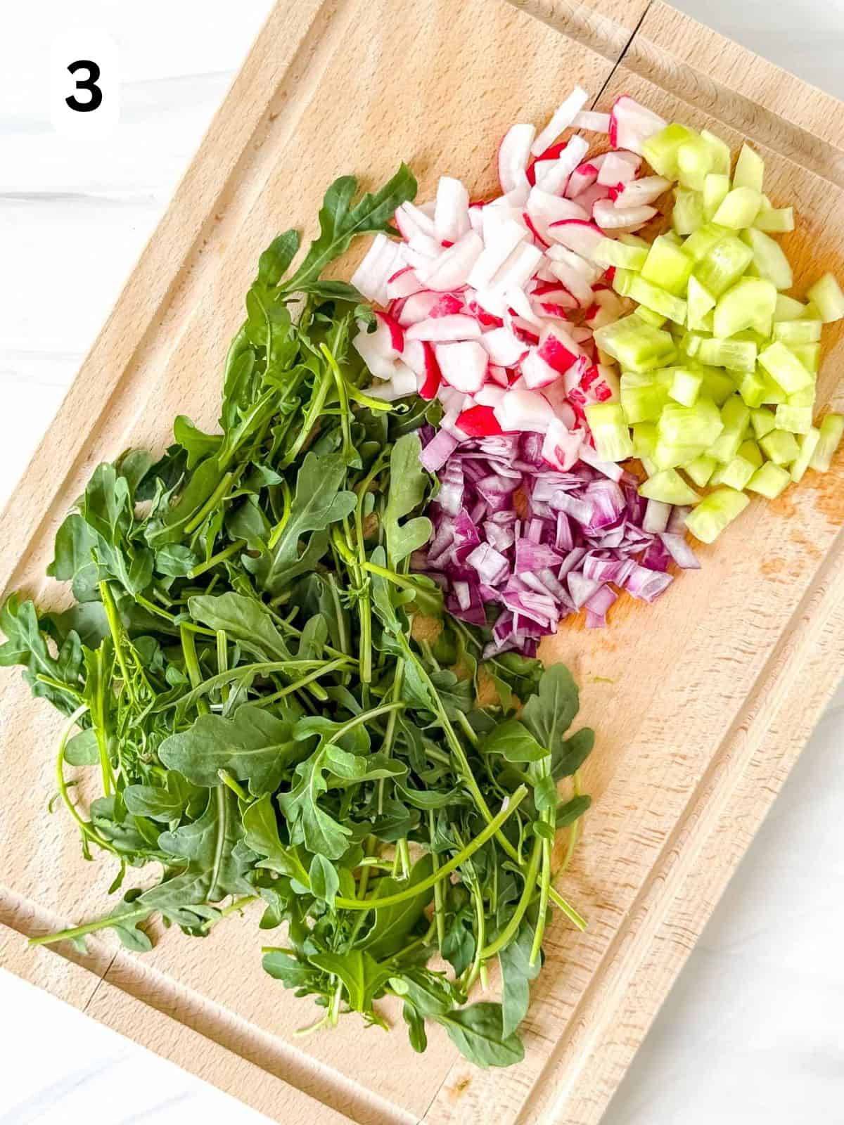 arugula leaves, diced radish, cucumber and red onion on a wooden chopping board labelled number three.
