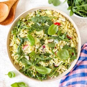arugula orzo salad with pesto in a bowl garnished with fresh basil leaves.