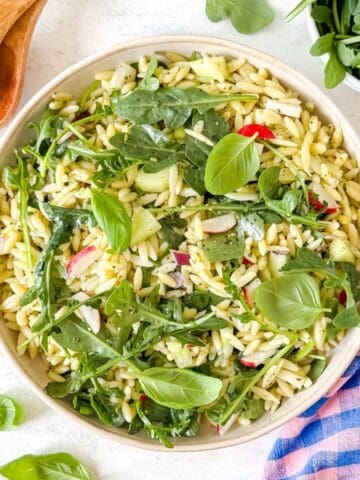 arugula orzo salad with pesto in a bowl garnished with fresh basil leaves.