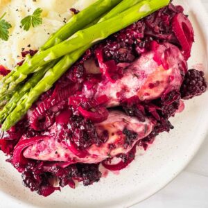 blackberry chicken on a white plate with asparagus and mashed potatoes.