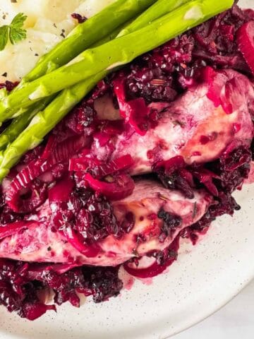 blackberry chicken on a white plate with asparagus and mashed potatoes.