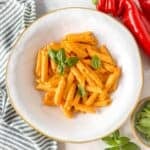 pasta with cottage cheese sauce in a white bowl garnished with fresh basil leaves and next to red sweet peppers.