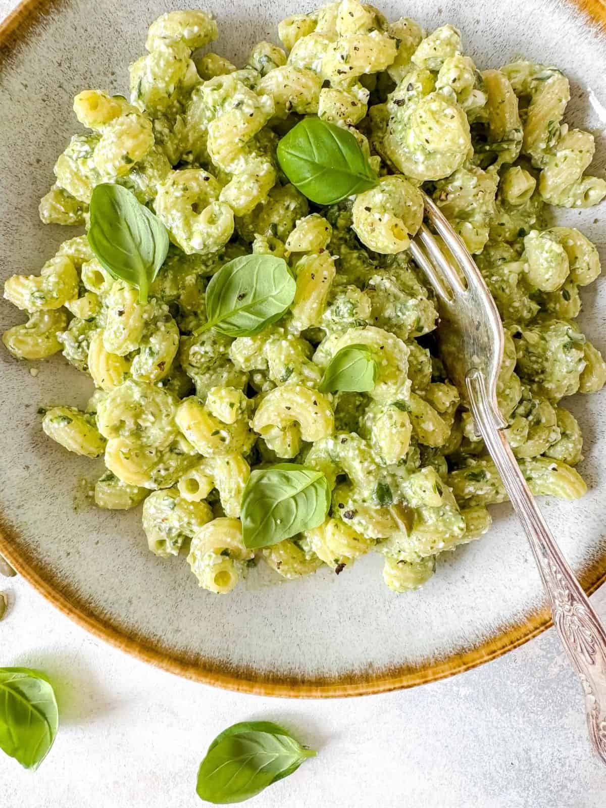 cottage cheese and pesto pasta in a bowl garnished with fresh basil leaves.
