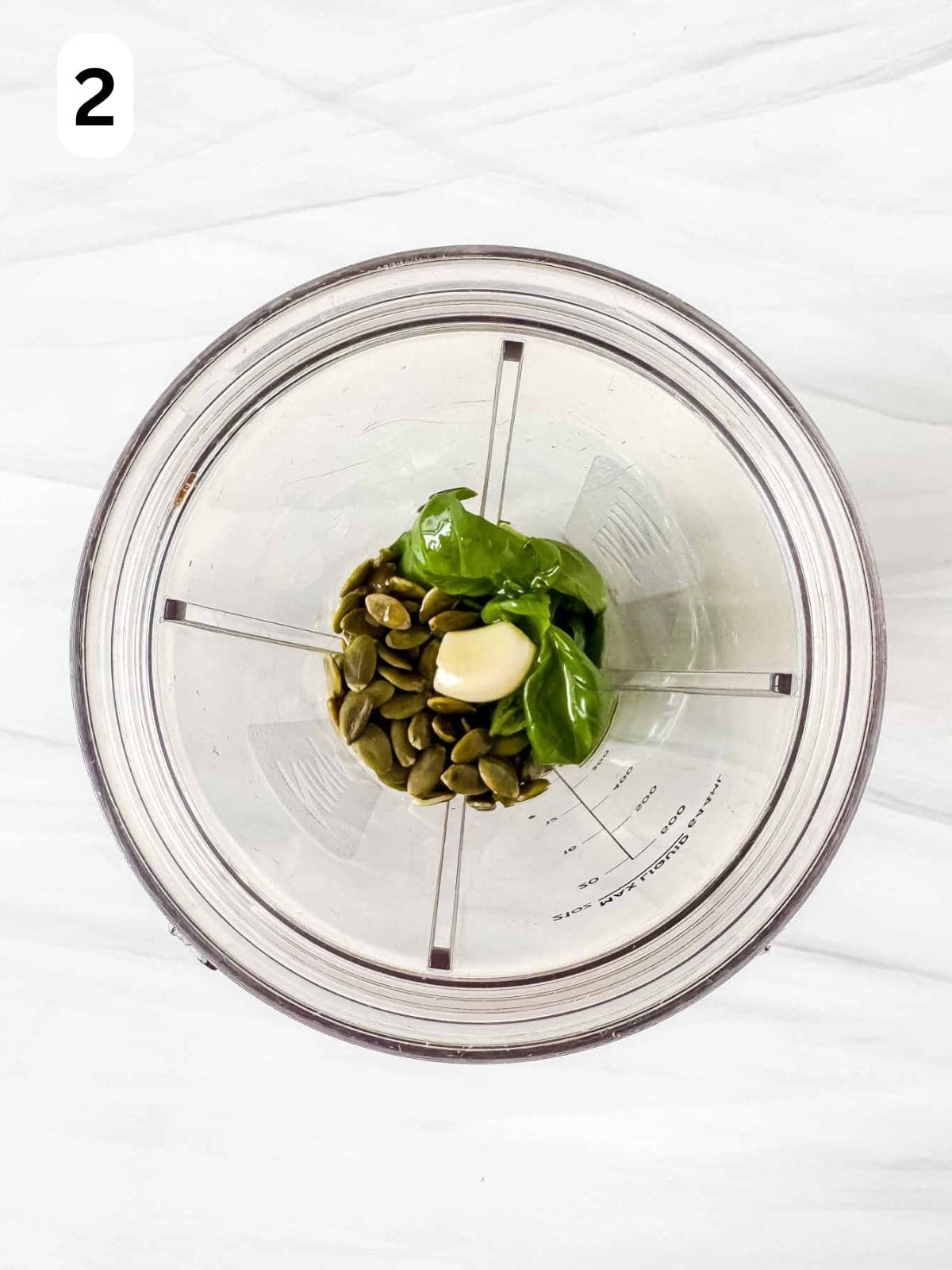pumpkin seeds, basil leaves, olive oil and garlic in a blender cup labelled number two.