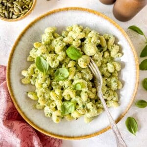 cottage cheese pesto pasta in a bowl garnished with fresh basil leaves, next to a small bowl of pumpkin seeds.