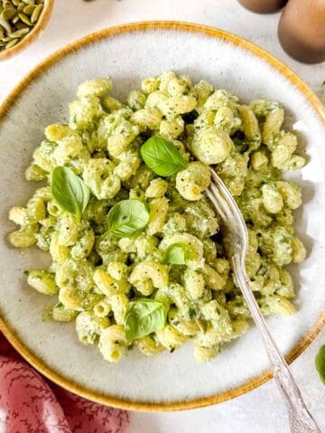 cottage cheese pesto pasta in a bowl garnished with fresh basil leaves, next to a small bowl of pumpkin seeds.