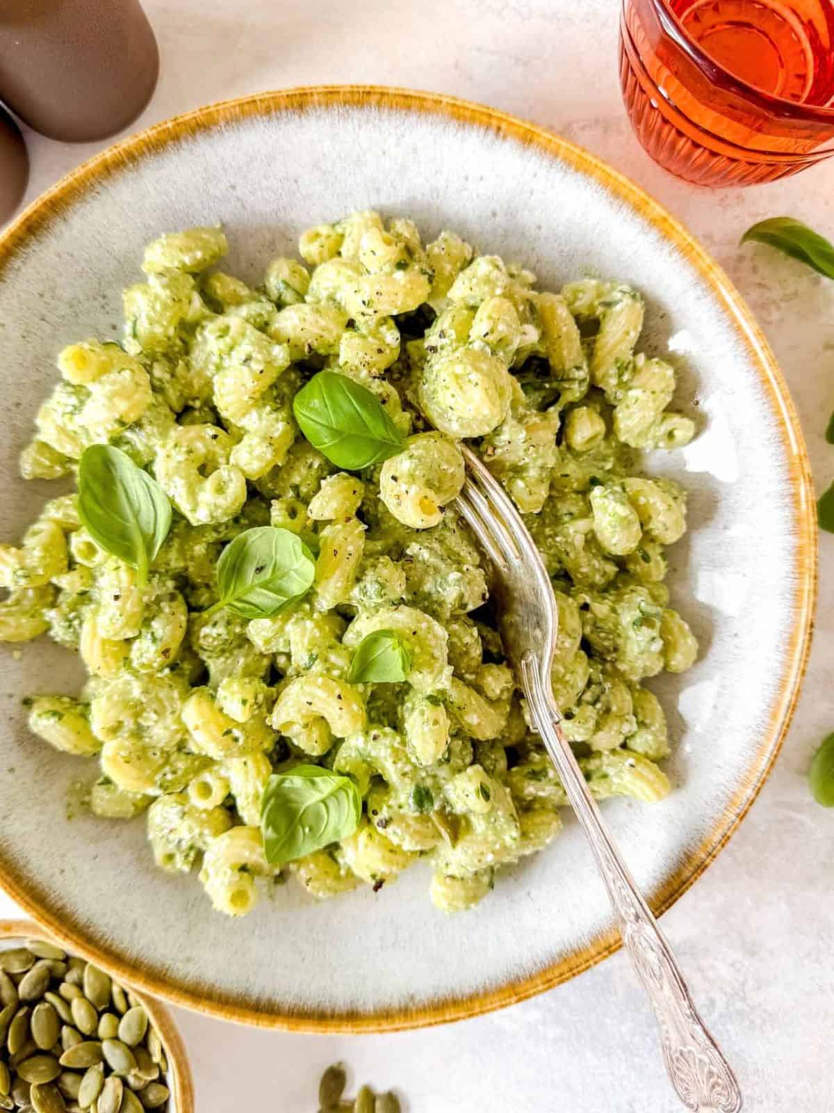 cottage cheese pesto pasta in a bowl next to fresh basil leaves and pumpkin seeds.