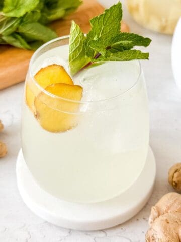homemade ginger beer without yeast in a glass garnished with fresh mint leaves and root ginger slices.
