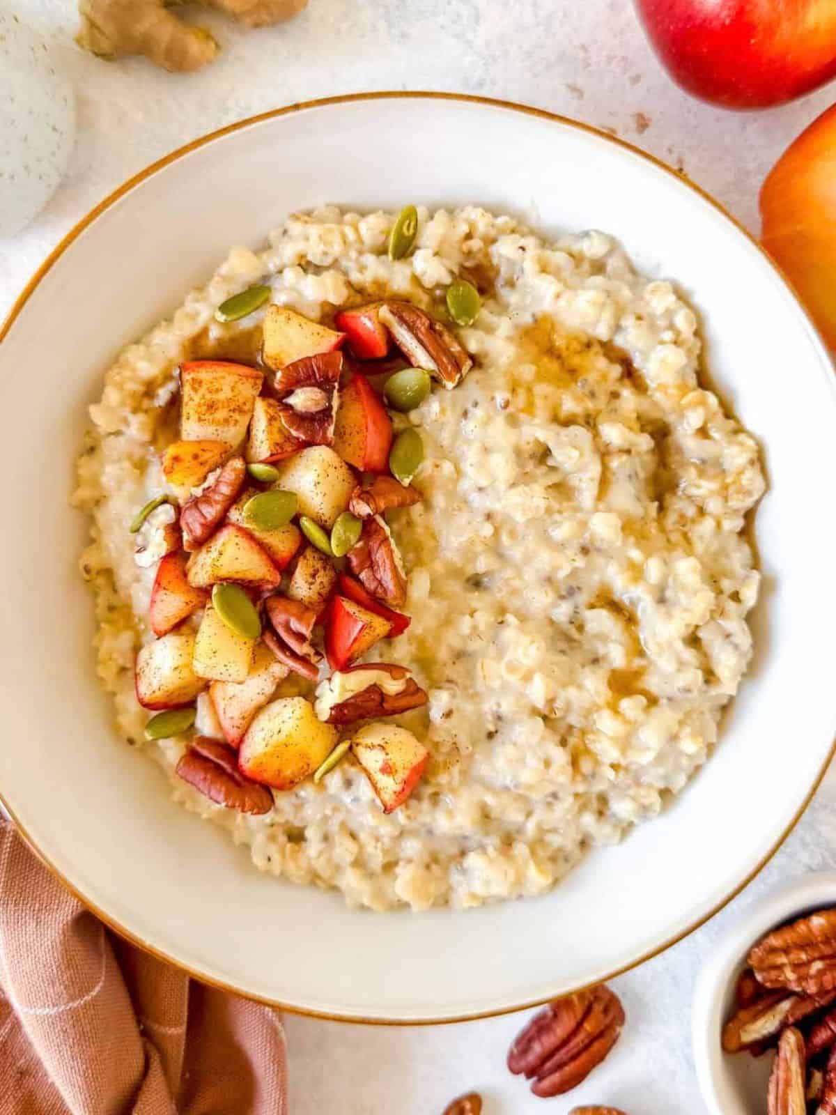 ginger oatmeal in a white bowl garnished with cooked apple, pecans and pumpkin seeds.